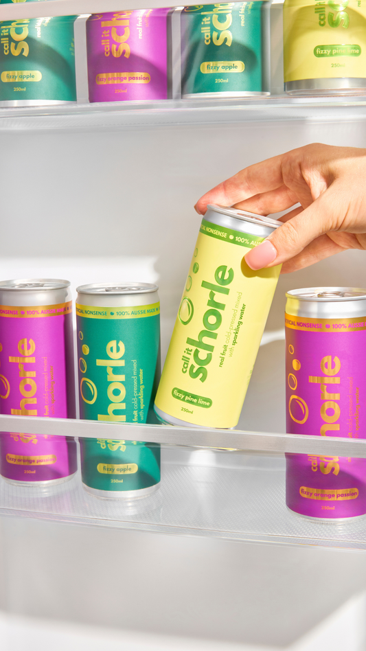 A brightly lit fridge stocked with colorful cans of schorle, a sparkling cold-pressed juice made from real fruits and veggies.